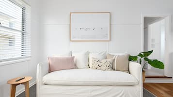 A white sofa with multiple cushions, a framed artwork above it, and a potted plant to the right.