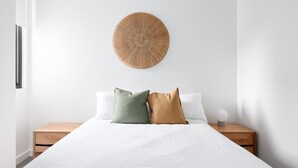 Quarto minimalista com uma cama grande, duas mesas de cabeceira, um pendurar redondo na parede e um abajur pequeno e branco.