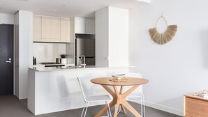 A modern kitchen with white cabinetry, a stainless steel refrigerator, and a round wooden table with two white chairs.