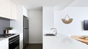 A modern kitchen with a stainless steel refrigerator, a built-in oven, a sink, and a wooden dining table.
