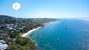 An aerial view of a coastal town with a beach, clear blue waters, and a lighthouse.