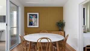 Un coin repas avec une table ronde et six chaises en bois, un tableau au mur et une plante en pot.