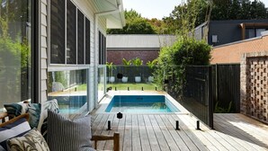 Un espace piscine extérieur moderne, doté d’une terrasse en bois, de murs en verre et d’un mur en briques.