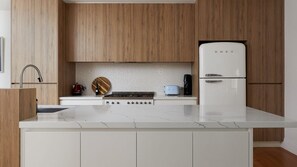 Une cuisine moderne avec des meubles en bois, un plan de travail blanc, une cuisinière, un réfrigérateur et une machine à café.
