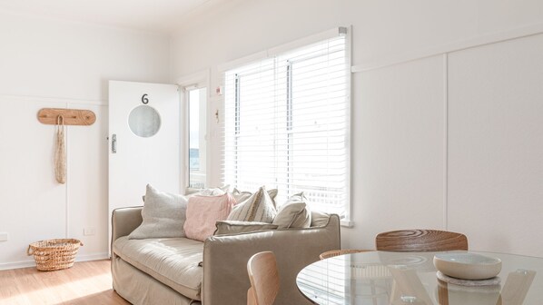 A modern living room with a sofa, a dining table, and a window with blinds.