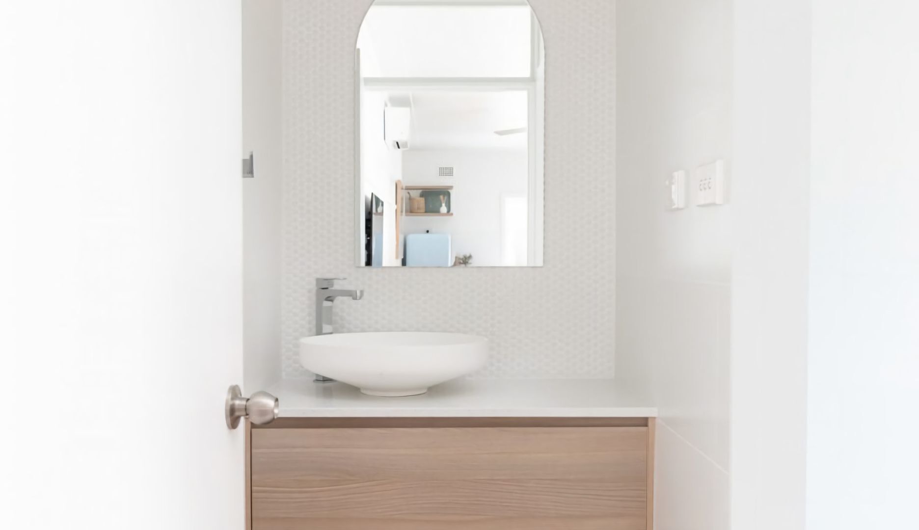 A bathroom with a white sink, a mirror above it, and a wooden cabinet below.