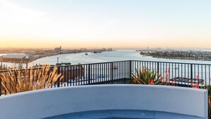 En balkon ved vandet med gelænder, der giver udsigt over en flod med både og industribygninger i det fjerne.