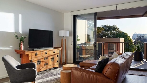 Un salon moderne doté d’un téléviseur à écran plat, d’un meuble en bois, d’un canapé en cuir et d’un balcon offrant une vue sur la ville.