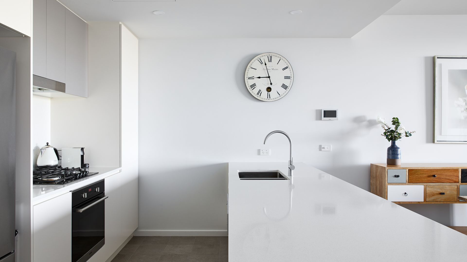 A modern kitchen with a white island, stainless steel appliances, a wall clock, and a small potted plant.