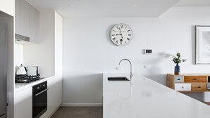 Une cuisine moderne avec un îlot central blanc, des appareils en acier inoxydable, une horloge murale et une petite plante en pot.