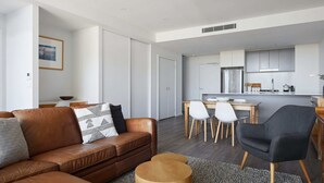 Un salon moderne avec un canapé en cuir marron, un fauteuil noir et un coin repas comprenant une table en bois et des chaises blanches.