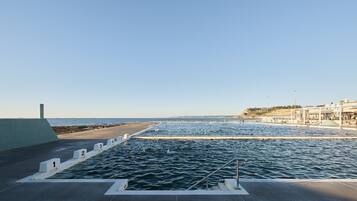 A swimming pool with numbered lanes, a viewing deck, and a beach in the background.
