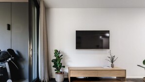 Ein modernes Wohnzimmer mit einem großen Flachbildfernseher an der Wand, einer Holzbank, einem Blumentopf und einem Fahrrad in der Ecke.