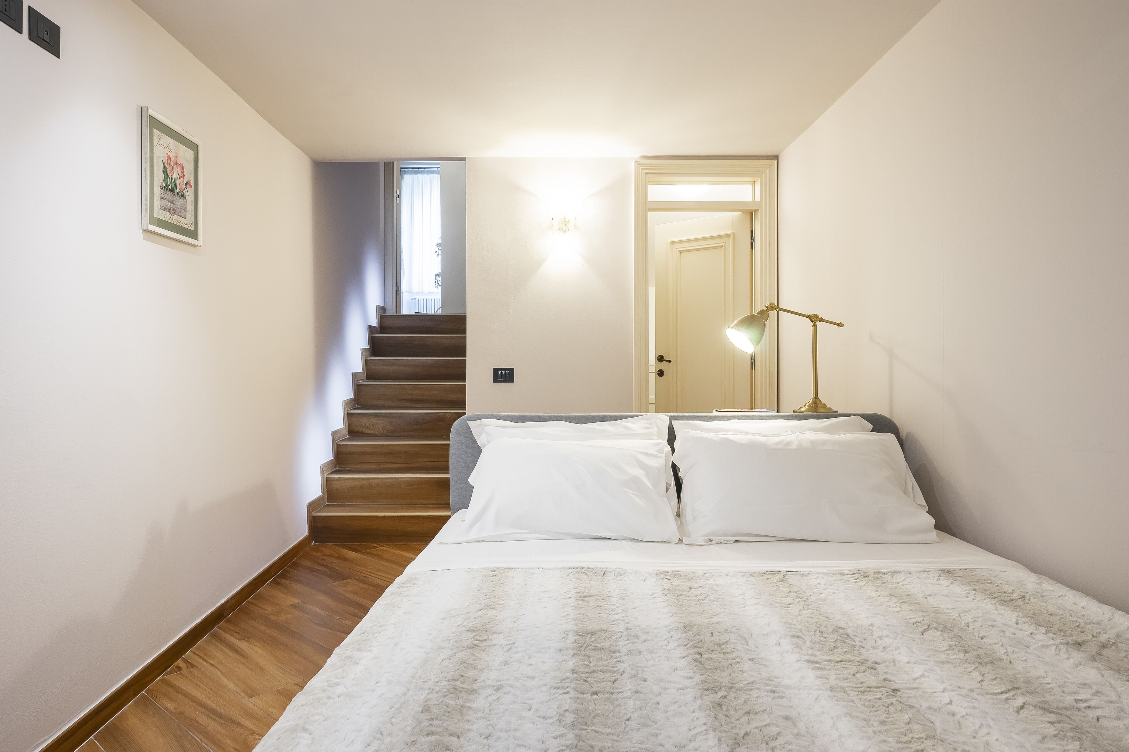 Een slaapkamer met een bed, een lamp en een trap naar een andere kamer.