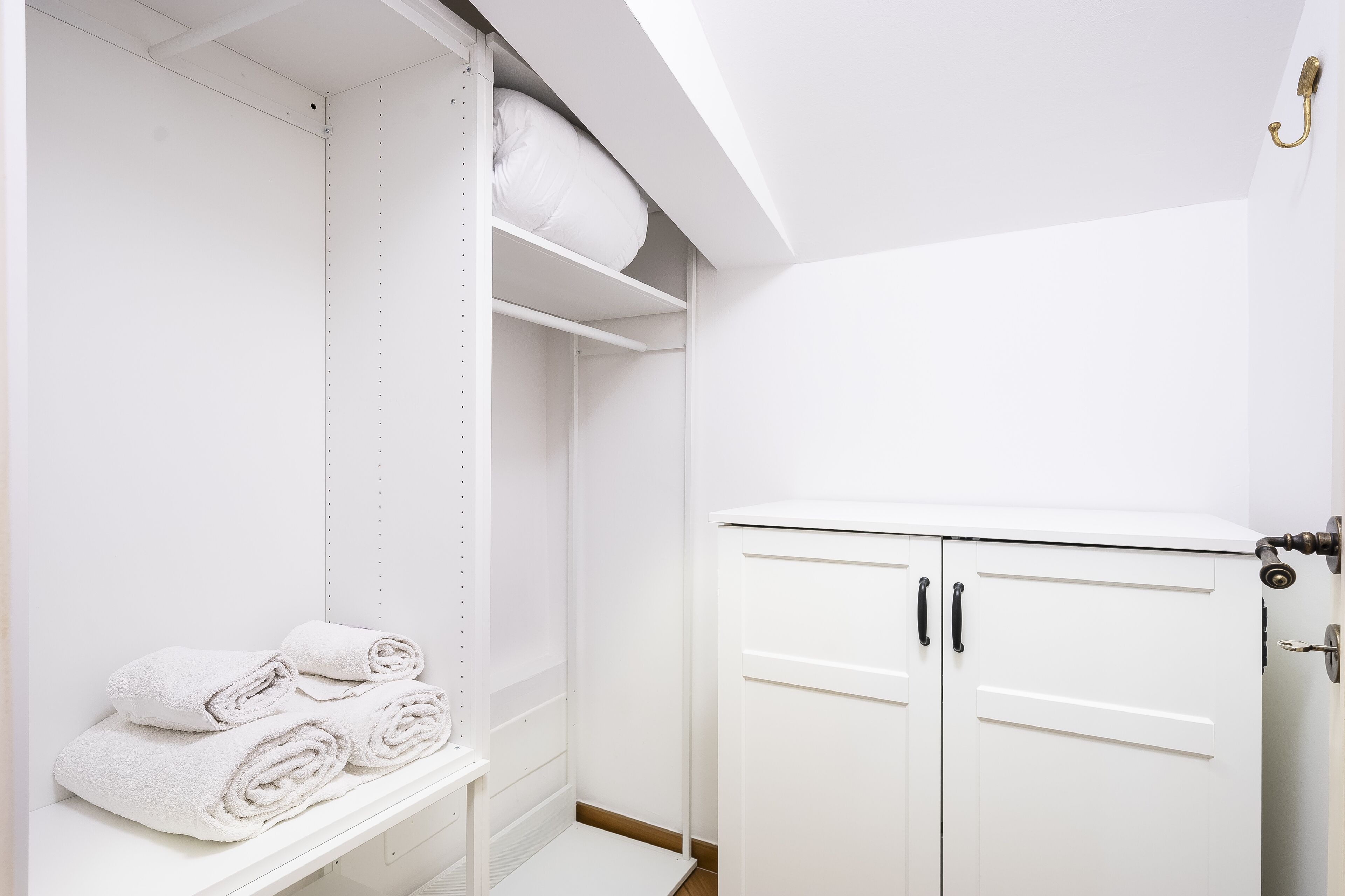 A white closet with shelves, a hanging rod, and a door with a lock.