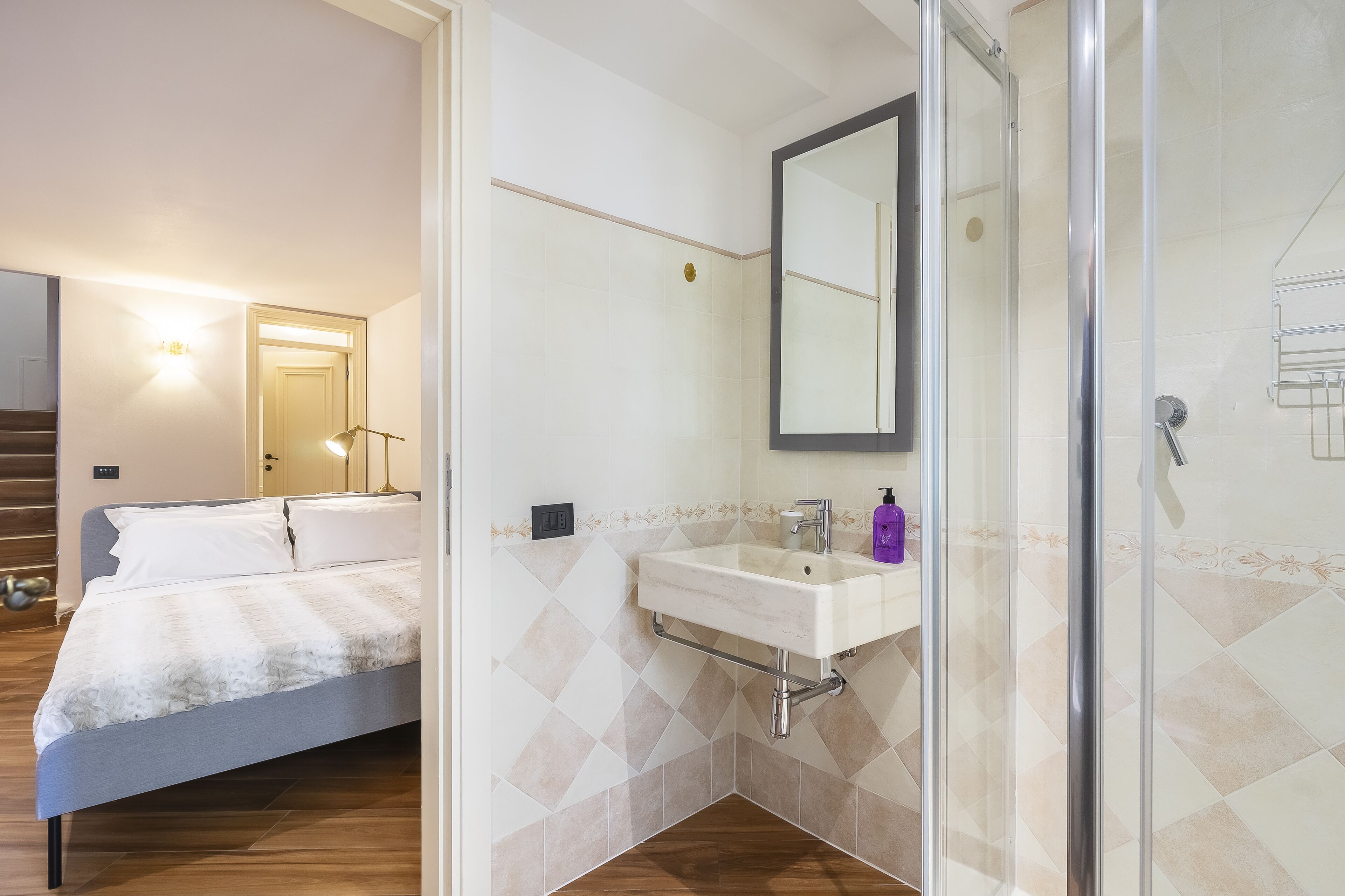 A bedroom with a bed, a bathroom with a sink and mirror, and a shower area.