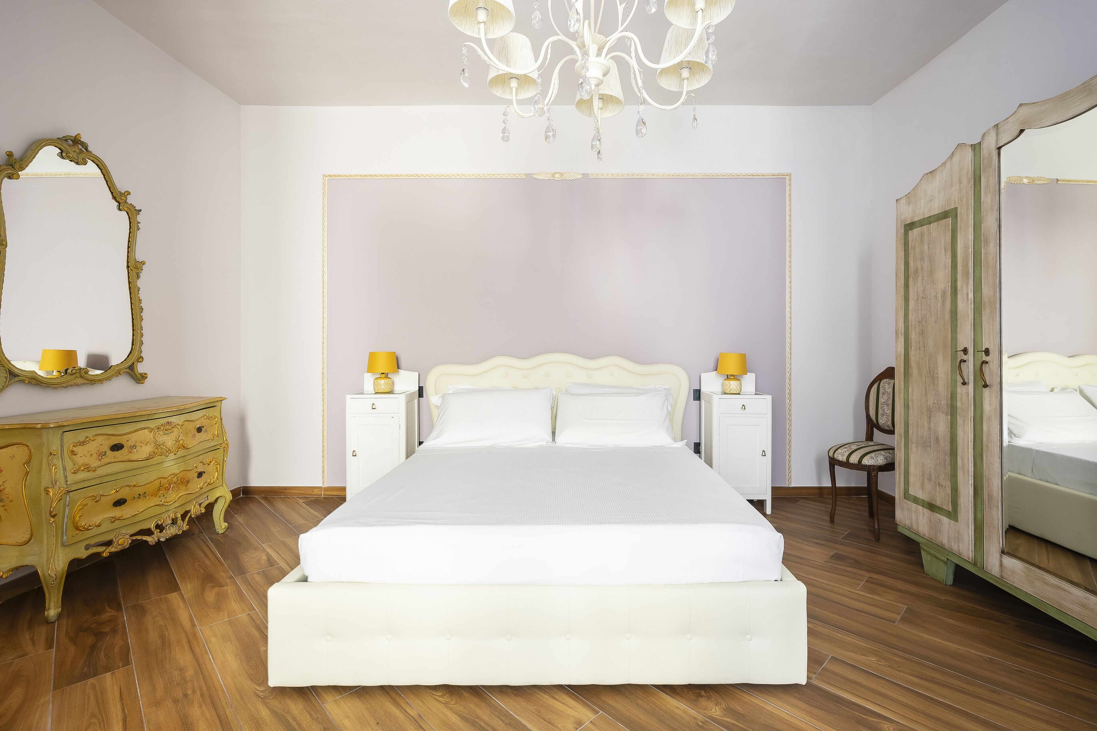 A bedroom with a large bed, a dresser, a wardrobe, and a chandelier.
