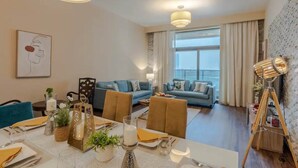 Una sala de estar moderna con comedor, que incluye un juego de sofá, una mesa de comedor para cuatro personas y un amplio ventanal con cortinas.