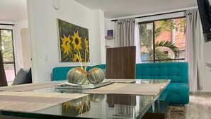 A modern living room with a glass dining table, teal sofa, and a painting of sunflowers. - Exclusivo Apartamento Privado Zona Rosa Sabaneta (Sabaneta)