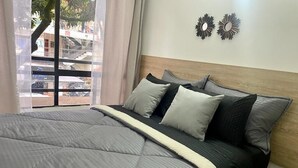 A bedroom with a large bed, grey bedding, a wooden headboard, and a view of the outside through a window. - Exclusivo Apartamento Privado Zona Rosa Sabaneta (Sabaneta)
