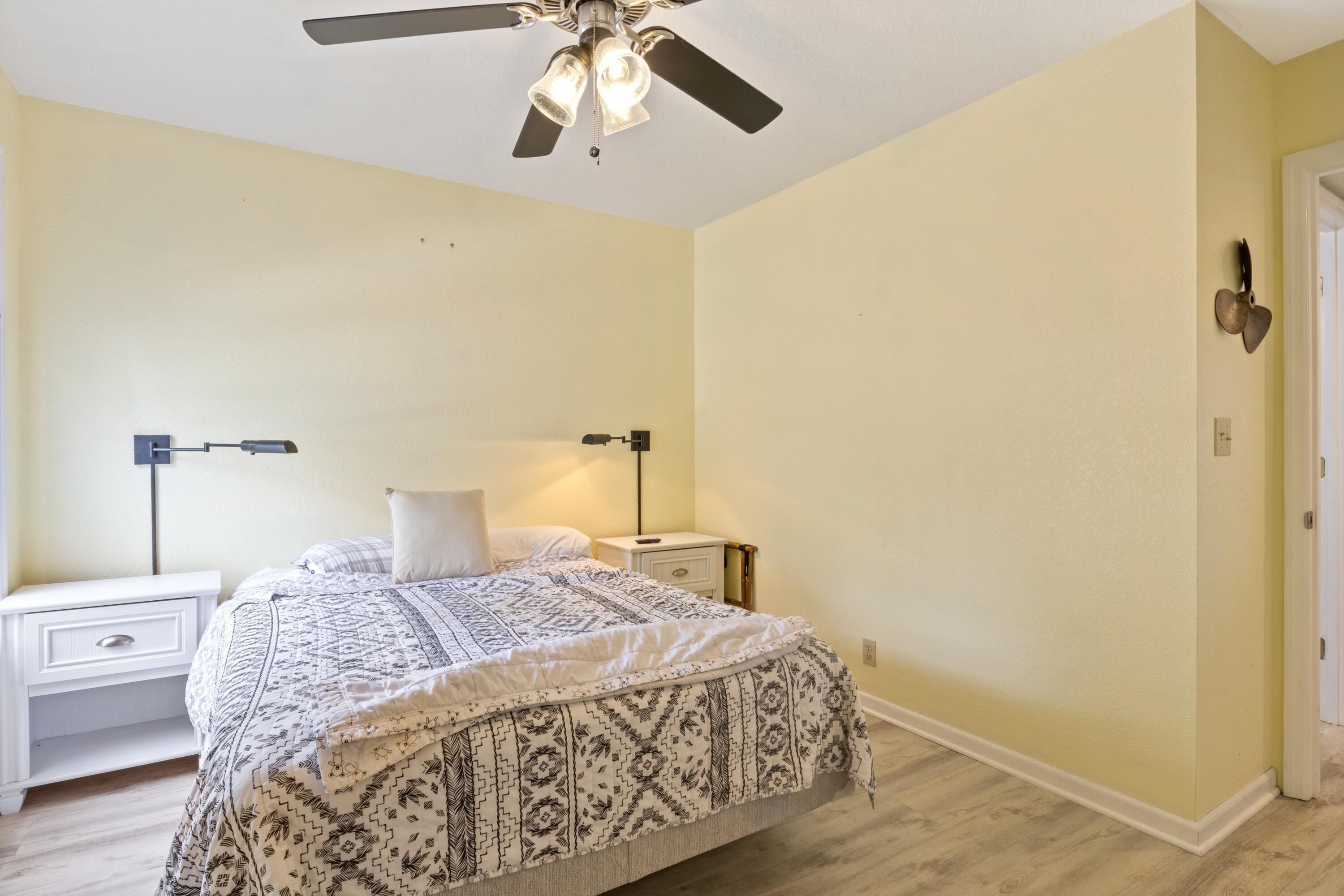 A bedroom with a bed, nightstands, a ceiling fan, and a door.