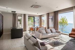 Enjoy a serene view of the sea from the large window in this stylish living room, featuring a dining area and comfortable seating.