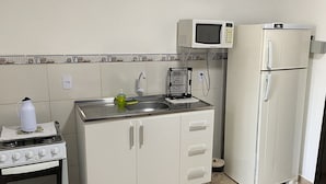 A kitchen with a stove, sink, microwave, and refrigerator. - Residencial Karine - Studio 05 (Joinville)