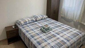 A bedroom with a bed, a nightstand, a wardrobe, and a window with curtains. - Residencial Karine - Studio 05 (Joinville)