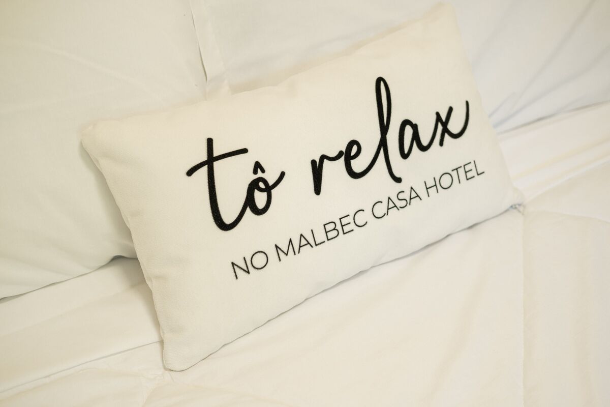 A pillow with the text "to relax" and "NO MALBEC CASA HOTEL" on a bed.