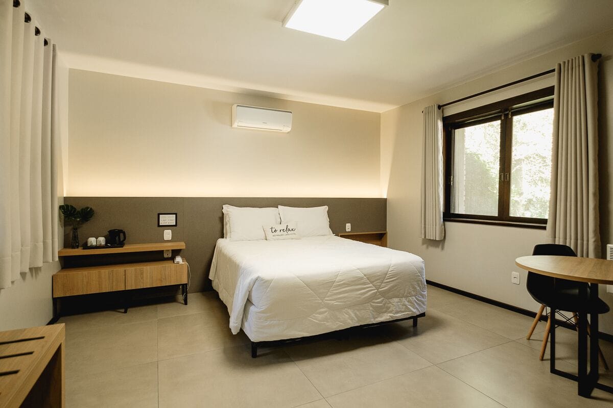 Een hotelkamer met een bed, een bureau, een stoel, een raam met gordijnen en een plafondlamp.