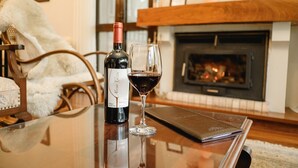 A bottle of wine and a glass on a table in a cozy living room with a fireplace.