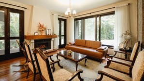A living room with a fireplace, leather sofa, wooden chairs, and large windows.