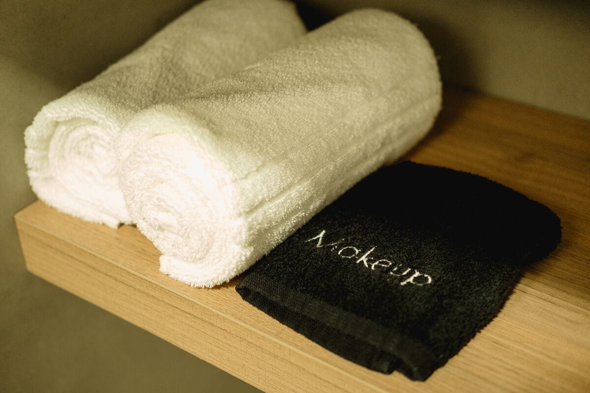 A wooden shelf with two white towels and a black towel with the word "Mokeyup" on it.