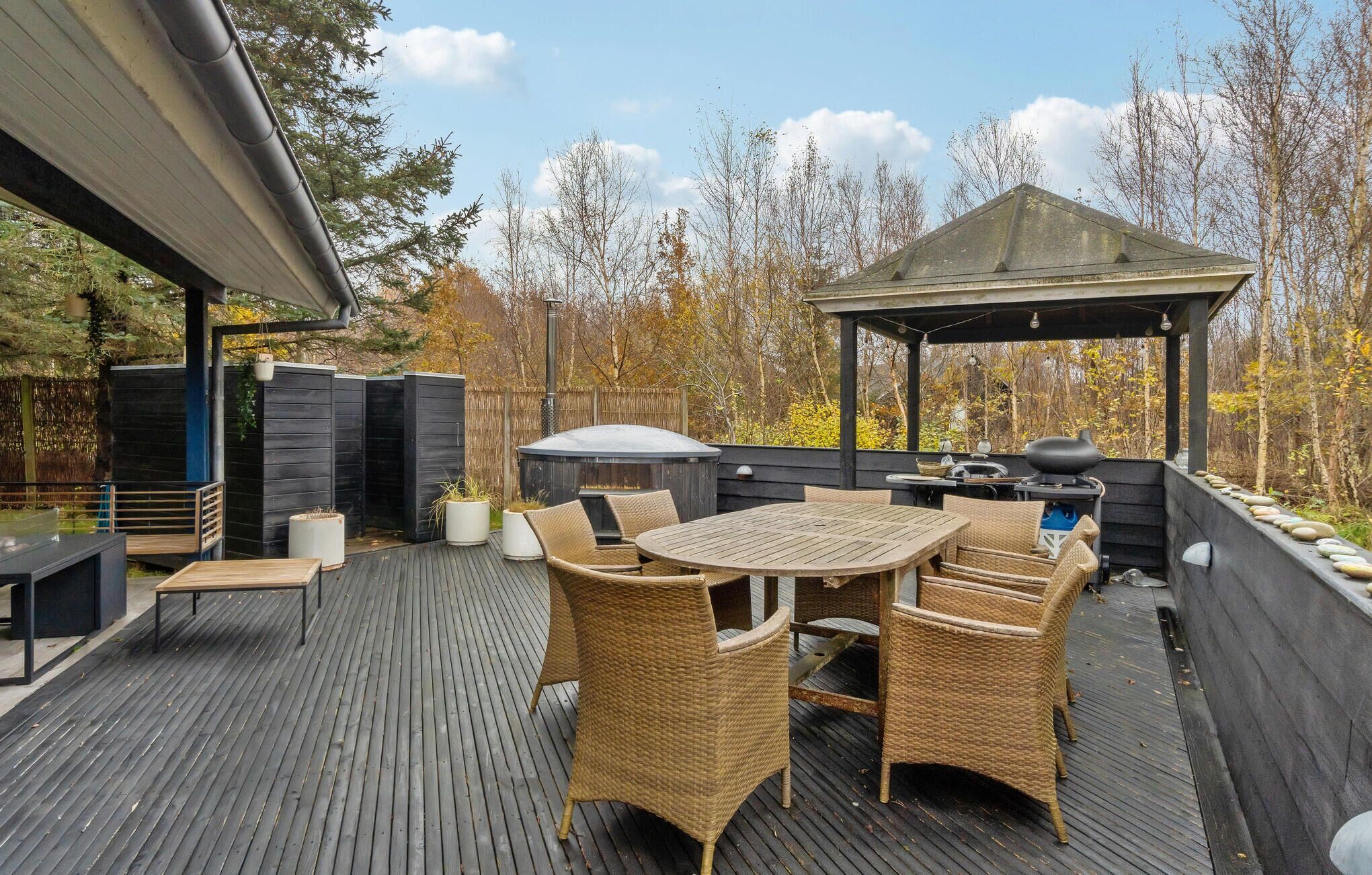 An outdoor deck with a round table and wicker chairs, a barbecue grill, and a gazebo.