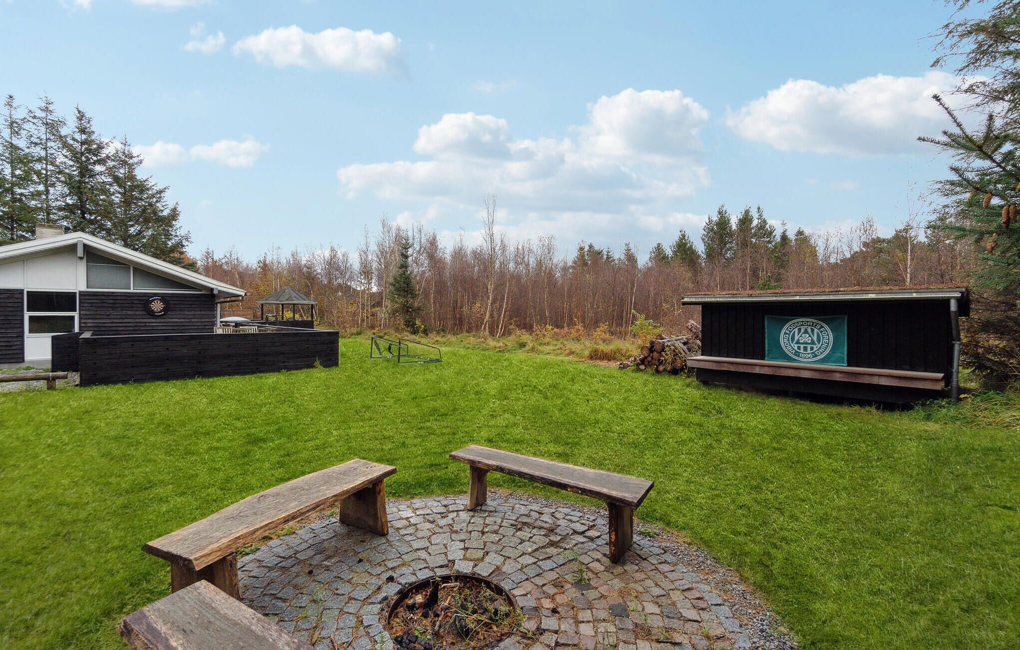 A backyard with a wooden bench, a fire pit, a small shed, and a house with a garage.
