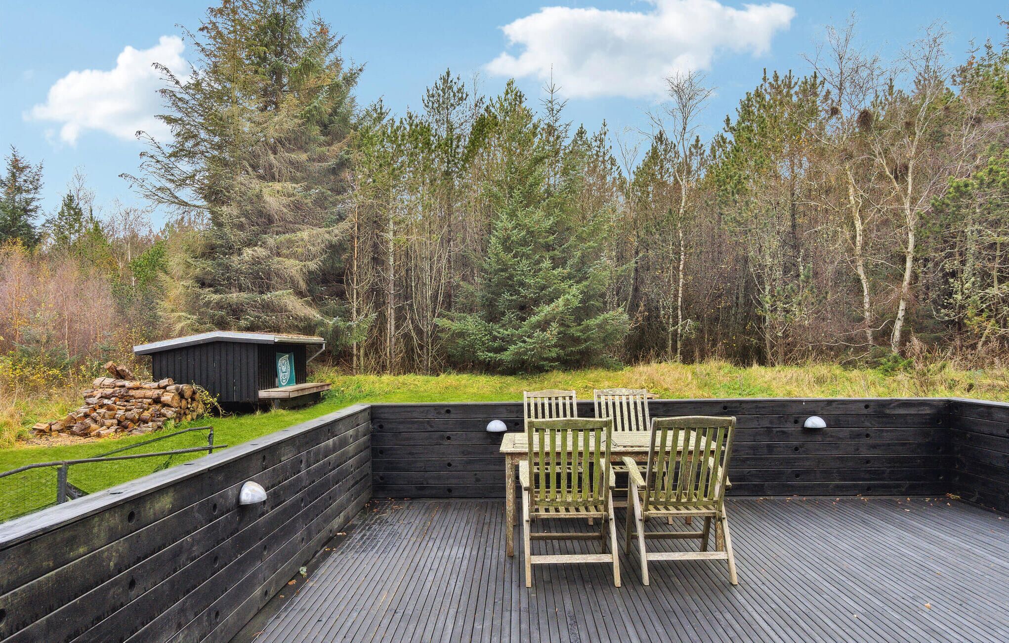 Une terrasse en bois avec deux chaises et un petit abri de jardin, le tout entouré d’une forêt.