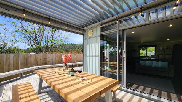 An outdoor patio with a wooden table, a vase with flowers, and a bottle of wine.