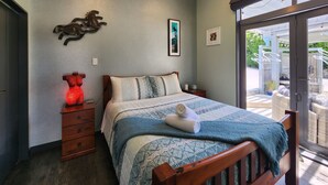 A bedroom with a bed, wooden nightstands, a red decorative item, and a view of the outdoor patio.