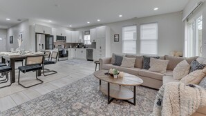A modern living room with a dining area, a sofa set, and a kitchen in the background.