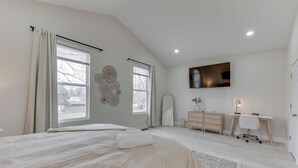 A bedroom with a large bed, a desk, a chair, a TV, and a dresser.