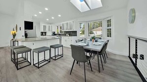 A modern kitchen with white cabinets, a central island, and a dining area with a table and chairs. - Huge CDA Getaway With Foosball And BBQ (Coeur d'Alene)