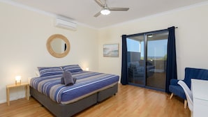 A bedroom with a bed, a bedside table, a mirror, a ceiling fan, and a view of the outdoors through a sliding glass door. - 120 Madaffari Drive - Featuring two master suites and a full outside bathroom (Exmouth)