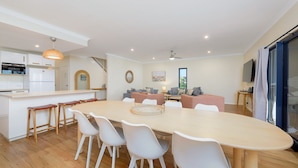 A modern kitchen with white cabinets, a dining area with a large table and chairs, and a living area with sofas and a TV. - 120 Madaffari Drive - Featuring two master suites and a full outside bathroom (Exmouth)