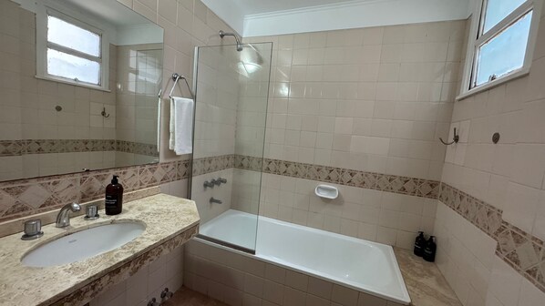 A bathroom with a glass-enclosed shower, two sinks, a bathtub, and a mirror. - Hotel BA Congreso (Buenos Aires)