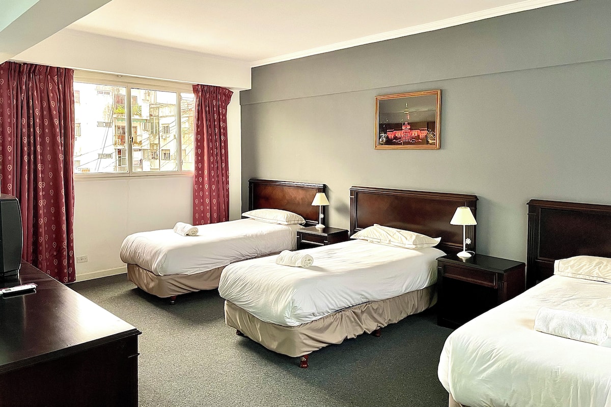 A hotel room with two beds, a desk, a TV, a window with curtains, and a painting on the wall.