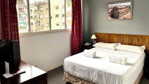 A hotel room with a bed, a desk with a TV, a phone, and a window with curtains. - Hotel BA Congreso (Buenos Aires)