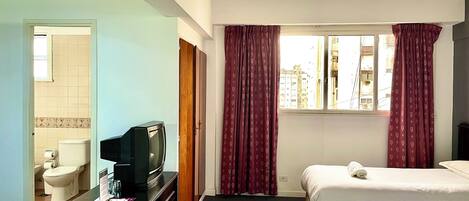 Habitación de hotel con cama, televisión, baño con inodoro y lavabo, y ventana con cortinas.