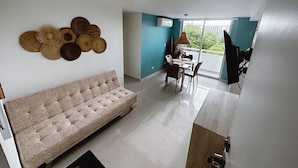 A living room with a sofa, dining table, chairs, and a view of the outdoors.