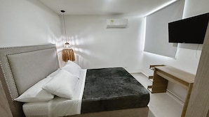 A bedroom with a bed, a desk, a television, and an air conditioning unit.