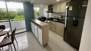 A modern kitchen with a stainless steel refrigerator, a microwave, and a gas stove. There is a small island with a sink and a chair.